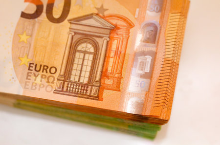 A stack of brown 50 euro banknotes lies on top of a stack of green 100 euro banknotes