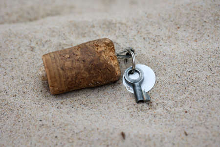 A key for a lock, padlock with a cork tag lies in the sand.