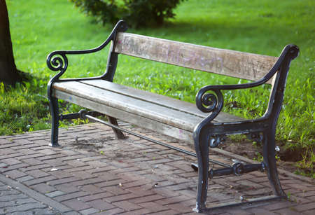 A cast iron park bench stands at the edge of a path in a park.の写真素材