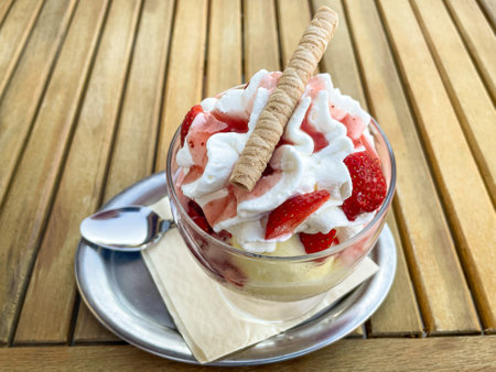 A strawberry sundae with whipped cream and waffle rolls on a table.の写真素材