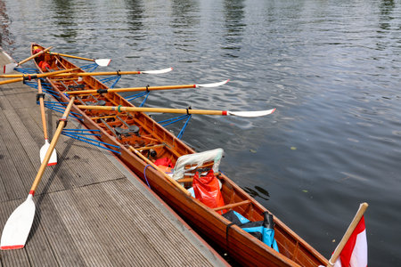 A rowing boat, multi-seater has moored to a jetty at a boathouse.