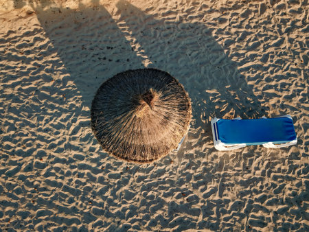 Stacked sun loungers and a parasol made of straw. Aerial view of a beach chair and coconut umbrella on the sandの写真素材