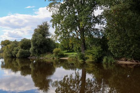 Autumn landscape with river, trees and blue sky with clouds.