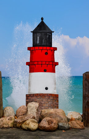 A lighthouse, stones and splashing water. Red and white lighthouse on the background of the sea and blue skyの写真素材