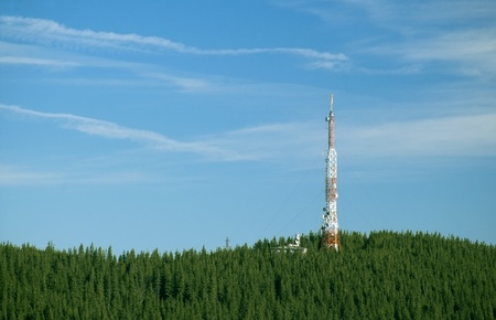 Telecommunication tower located on a forested hilltop towering into the sky against blue skyの写真素材
