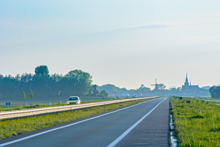 Road in Netherlands with village and windmill in backgroundの写真素材