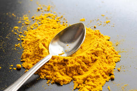 The metal spoon is on a yellow turmeric slide. Black background. Spice. Seasoning for dishes.