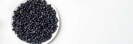 Blue delicious blueberries in a white plate on a white background top view