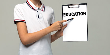 Student's hand shows a pen on paper with the word education, business and scool concept, isolated on light gray background.の写真素材