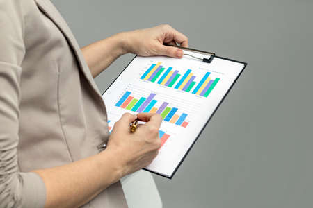 Woman looking at graph on clipboard on gray background. Director pointing with pen to board. Business education conceptの写真素材