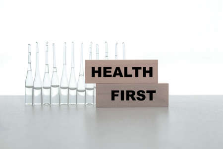 The word HEALTH FIRST is made card on a white background with ampoules. Medical concept.の写真素材