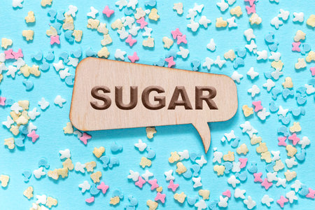 The word sugar is carved into a wooden callout or message on a blue background with sugar figurines. Medicine and health maintenance concept.の写真素材