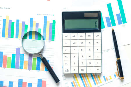 The magnifying glass lies on papers with color charts, pen and calculator on white background....