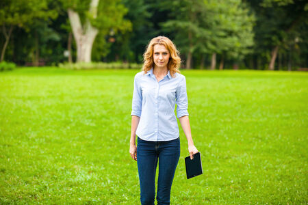 young beautiful woman with tablet in hand, in walking in the parkの写真素材