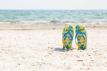 Pair of colored sandals on a white sand beach in front of the sea. The right place for relaxation and vacationsの写真素材
