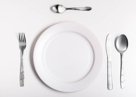 Plates with a silver fork, spoon, dessert spoon and a knife isolated on whiteの写真素材