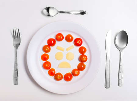 angry emoticon food, made from cheese and tomatoes on a plate with cutlery, isolatedの写真素材