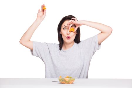 young natural expressive woman playing with her healthy food, orange and kiwi, isolated on whiteの写真素材