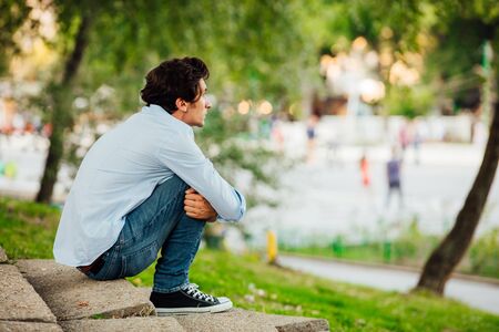 adult man in blue shirt sitting alone on stairs outside and thinking
