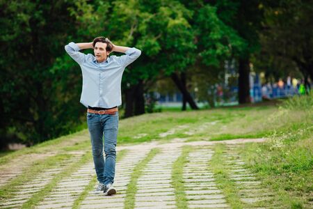 young adult in blue shirt and jeans walking alone in parkの写真素材