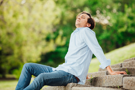 adult man in blue shirt sitting alone on stairs outside and thinkingの写真素材
