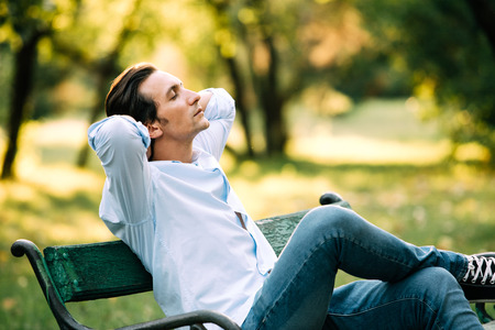 atractive adult man sitting alone on bench in parkの写真素材