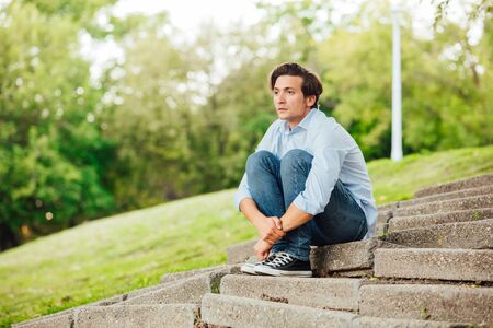 adult man in blue shirt sitting alone on stairs outside and thinkingの写真素材