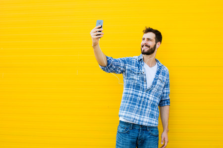 young happy man casual dressed with headphones and smart phone on yellow backgroundの写真素材