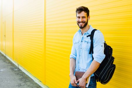 handsome student with bakpack and a book on yellow background