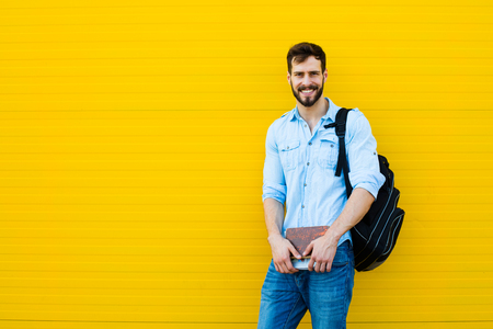 handsome student with bakpack and a book on yellow backgroundの写真素材