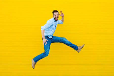 handsome man casual dressed celebrating and jumping on yellow backgroundの写真素材