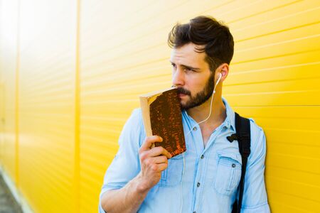 handsome student with bakpack and a book on yellow backgroundの写真素材