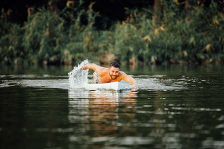 handsome athletic man swimming on a paddleboard and smiling, lake surrounded by trees
