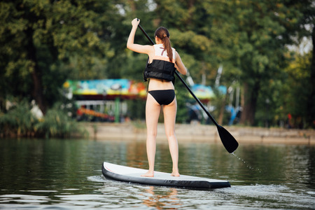 athletic woman doing paddleboarding on a lake surrounded by treesの写真素材