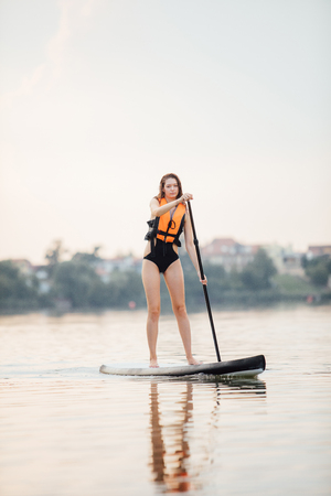 athletic woman doing paddleboarding on a lake surrounded by treesの写真素材