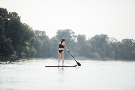 athletic woman doing paddleboarding on a lake surrounded by treesの写真素材