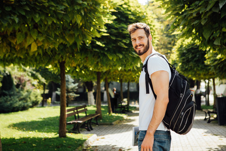 handsome student having books in hands and backpack standing outsideの写真素材