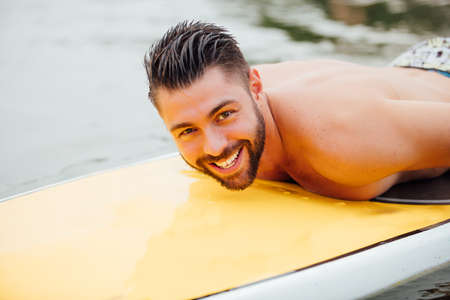 handsome athletic man swimming on a paddleboard and smiling, lake surrounded by treesの写真素材