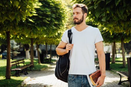 handsome student having books in hands and backpack standing outsideの写真素材