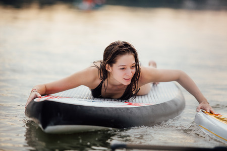 woman lying and relaxing on a paddle board on a lake surrounded by treesの写真素材