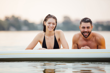 lovers man and woman relaxing in water on a paddleboard and smilingの写真素材
