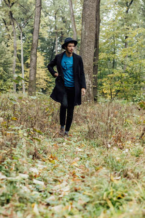 young man with black hat walkink in forest
