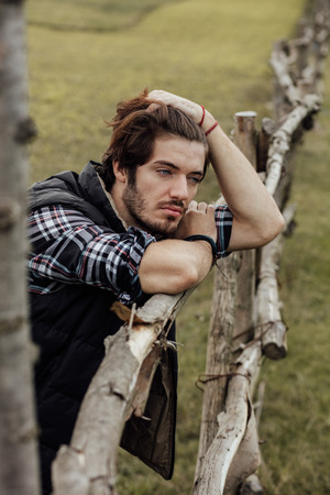 young sexy country boy next to a wooden fence, standing outside in nature