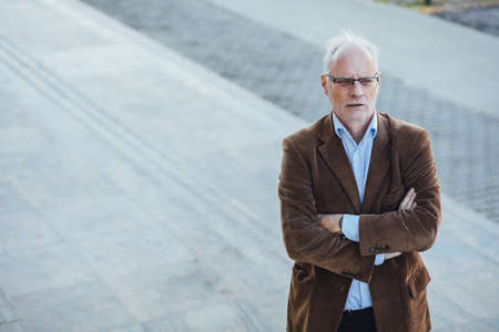 adult person with gray hair and eyeglasses elegant dressed, outside on the steps of an office buildingの写真素材