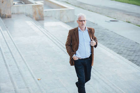 adult person with gray hair and eyeglasses elegant dressed, outside on the steps of an office buildingの写真素材