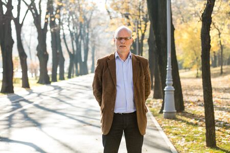 old elegant man standing outside on  the street with hands at backの写真素材