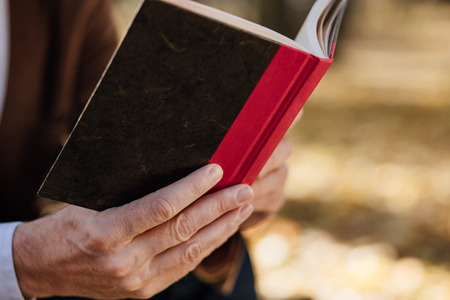 old elegant man with gray hair reading a book outside in parkの写真素材