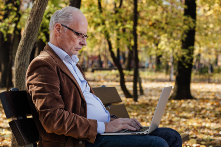 old businessmen sitting outside on a bench and working at laptopの写真素材