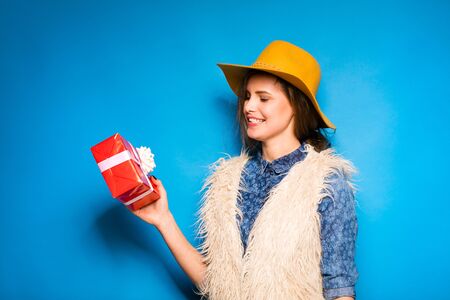 young modern woman holding a red gift in hands, on blue background