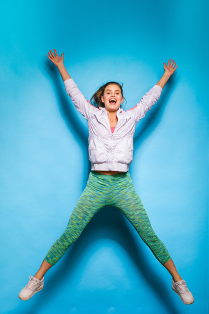 young athletic woman in fitness equipment jumping on blue backgroundの写真素材